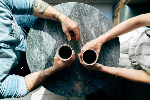 two people sitting at table with coffee - only see arms