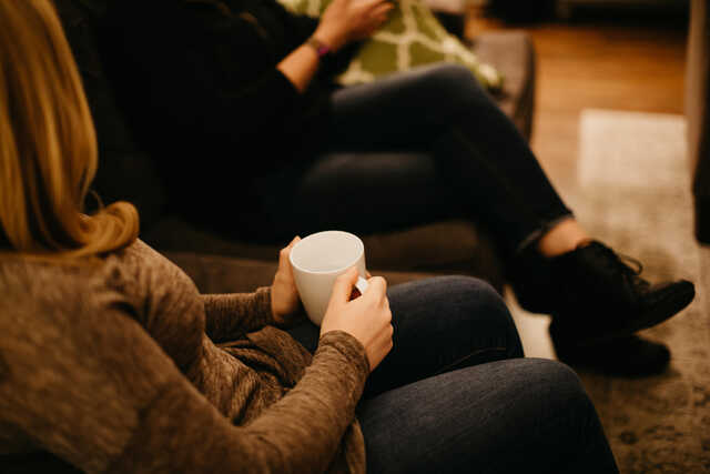 two women chatting on a couch drinking coffee