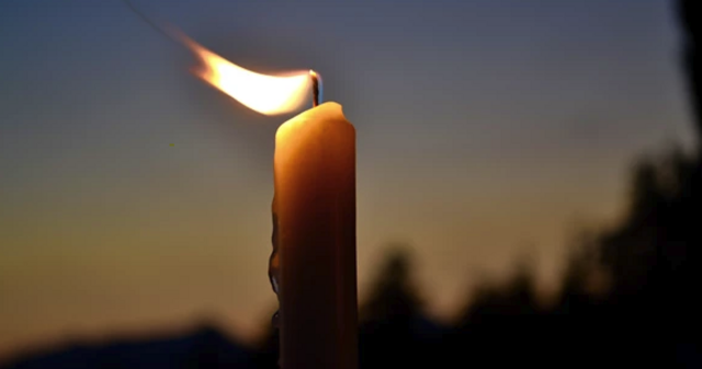 lit candle with flame blowing in the wind outside