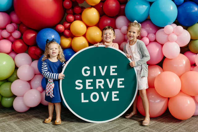 children in front of balloons with a give serve love sign