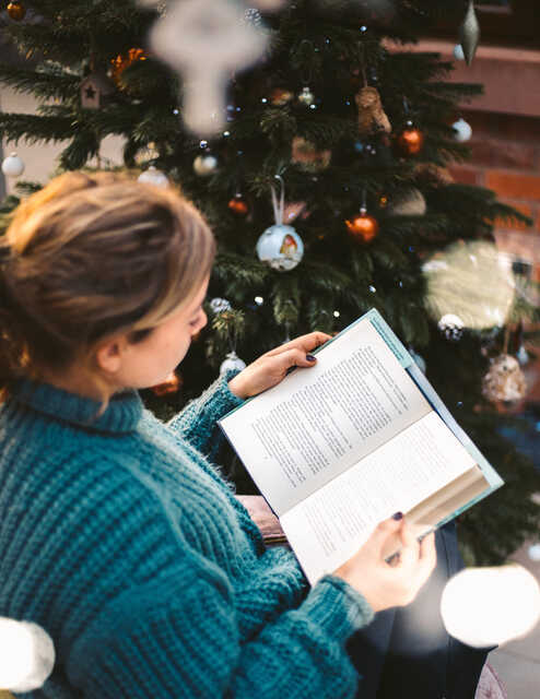 woman reading a book next to a christmas tree
